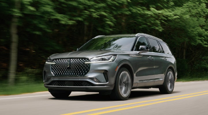 A 2027 Lincoln Aviator® SUV is being driven down a road lined with trees. | South Bay Lincoln in Hawthorne CA