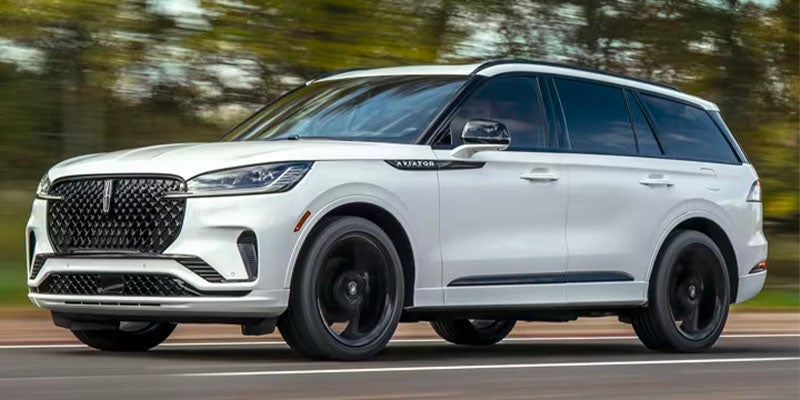 A sleek three-row luxury Lincoln Aviator SUV with bold grille and dynamic side profile in motion.