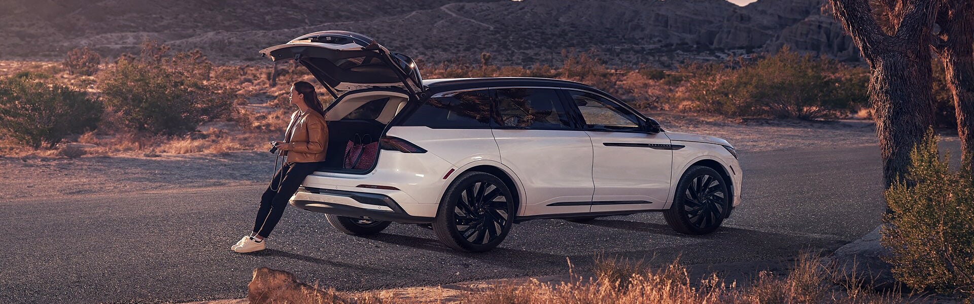 A Lincoln SUV is parked on a desert highway with rocky hills in the background.